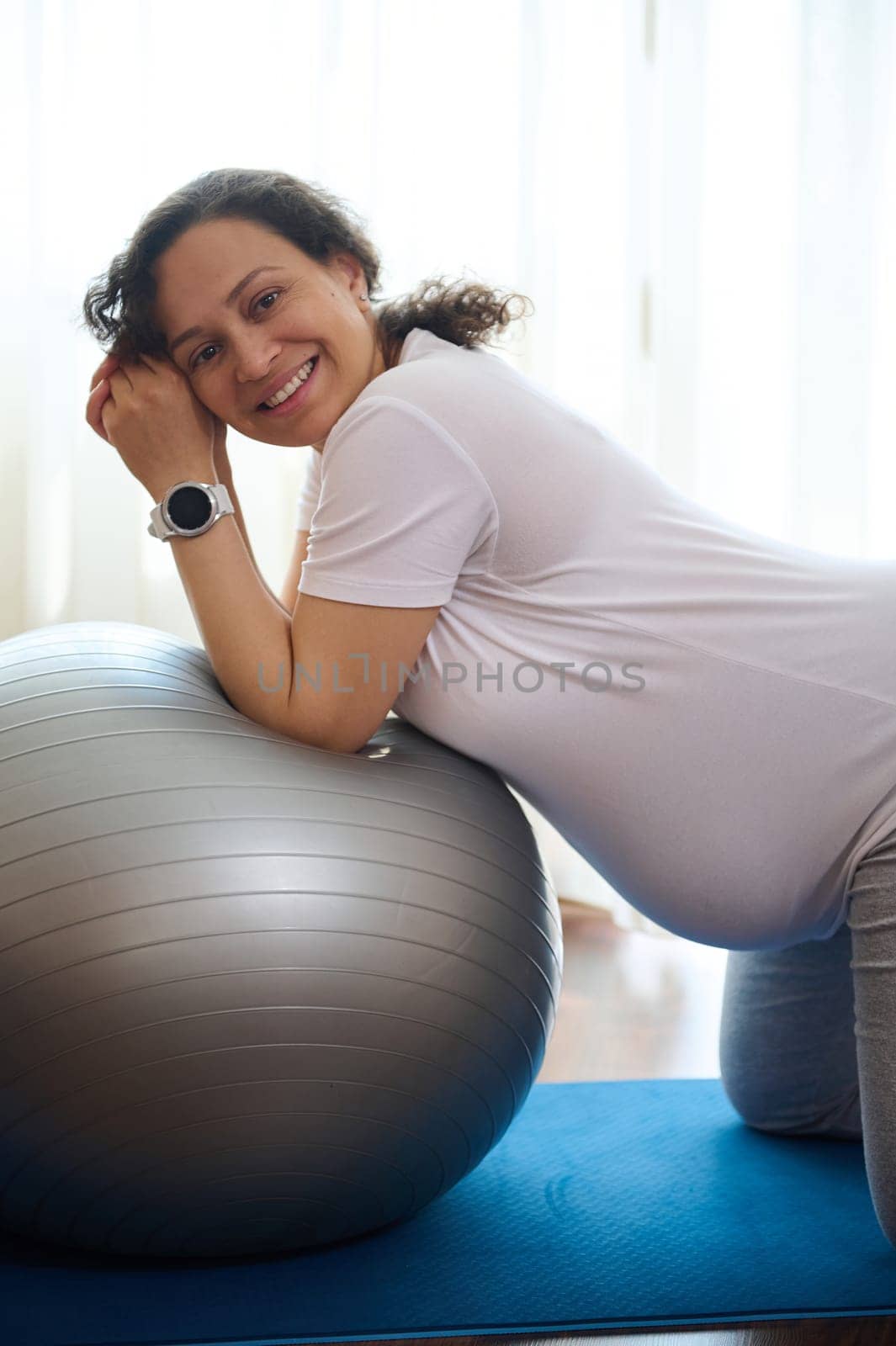 Happy pregnant woman smiling, looking at camera, exercising with a fit ball at home. Pregnancy. Maternity lifestyle by artgf