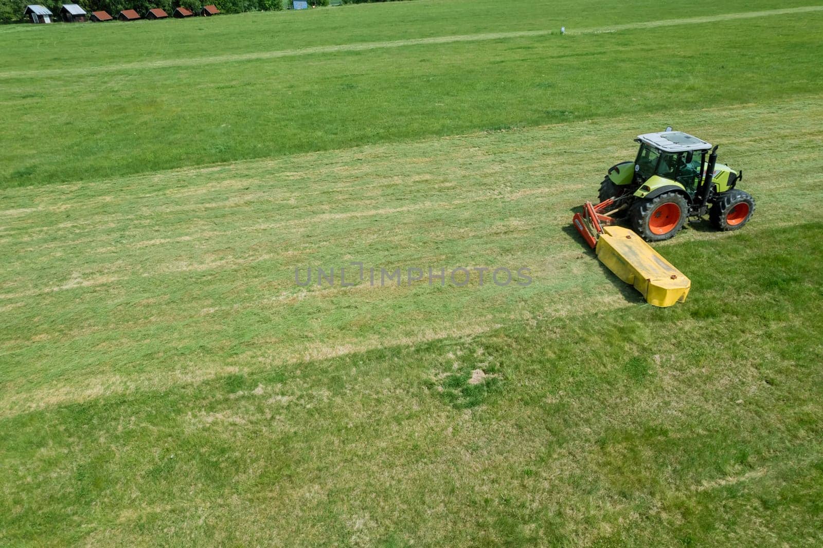 Field is being neatly mowed by the tractor's rotary cutter. Rotary mower attached to tractor is responsible for cutting grass.
