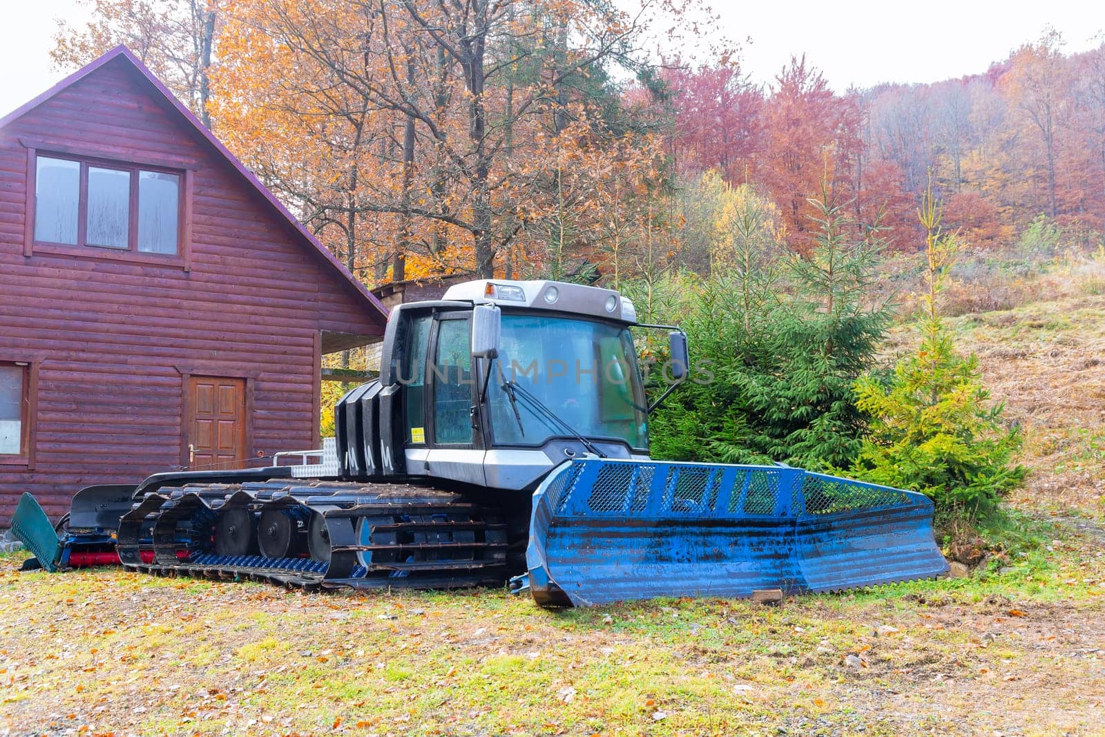 Crawler tractor near wooden house in mountains ready for snow collection that clean snow over ski tracks.