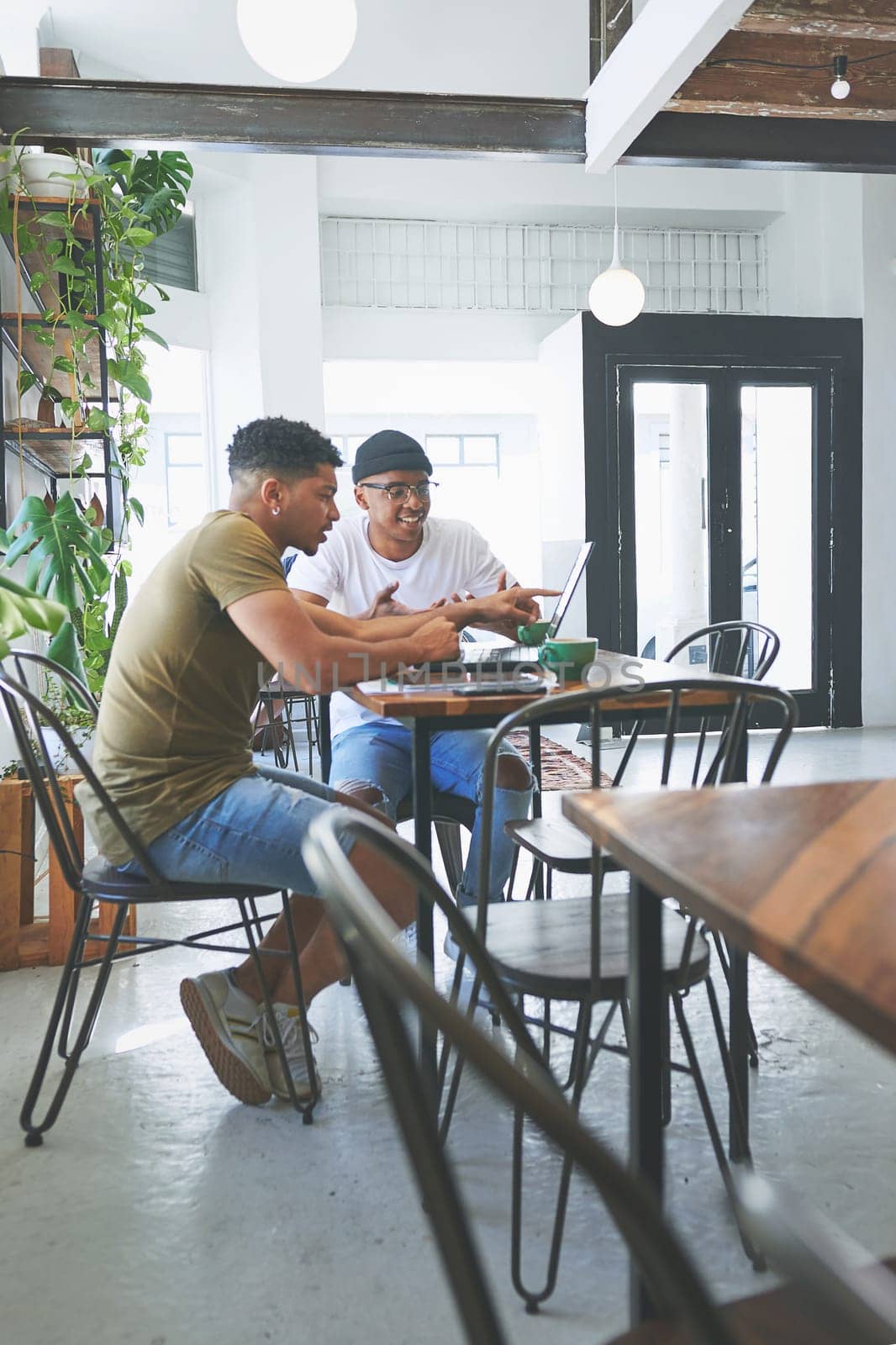 This idea would go great with our business model. Full length shot of two handsome friends sitting together in a coffeeshop and using technology during a discussion