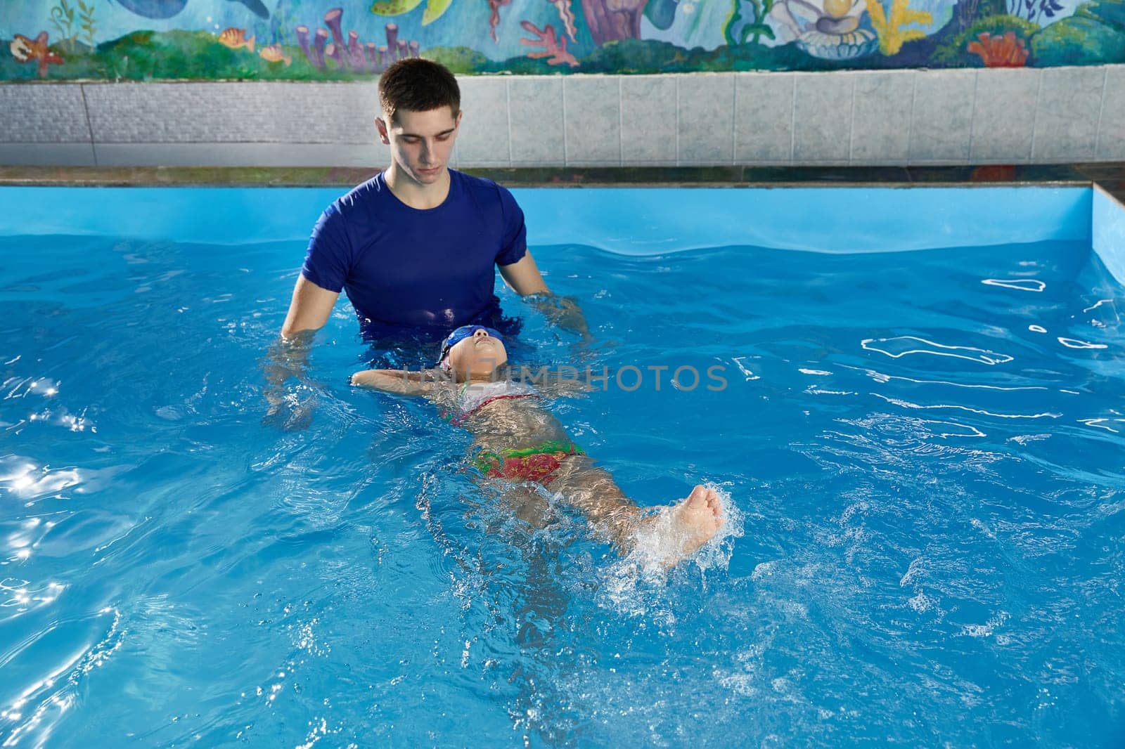 Little girl learning how to swim in pool with teacher by Mariakray