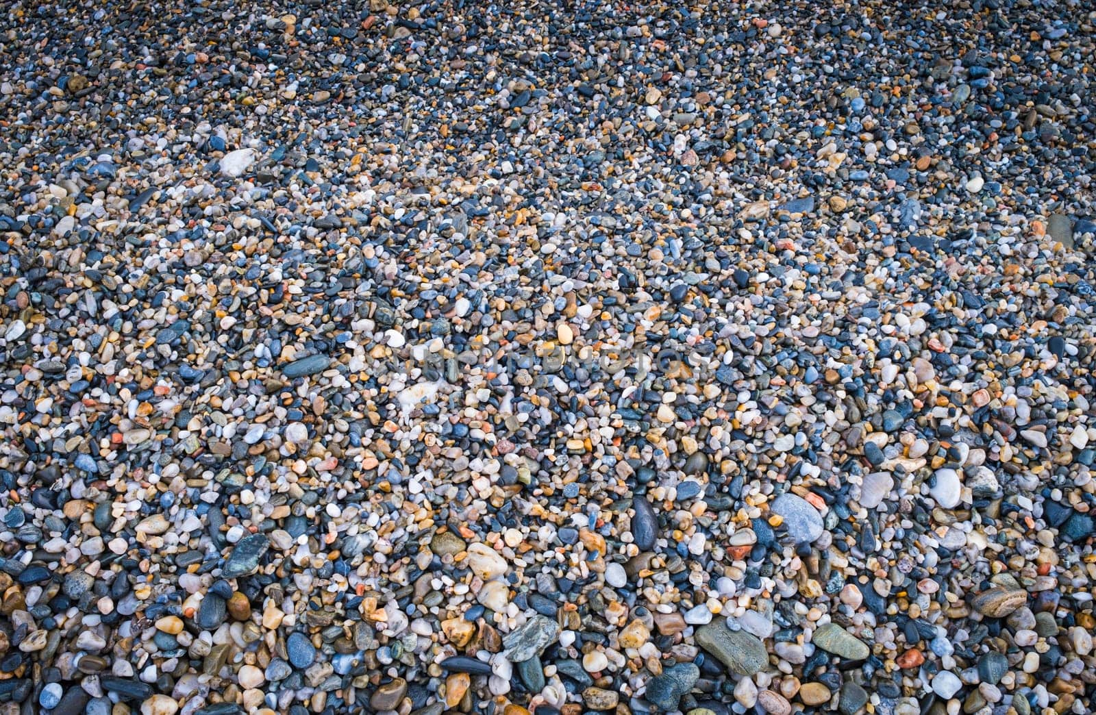 Close-up of the Smooth and Rounded Pebbles Texture on Sandy Beach Shoreline with Natural Light