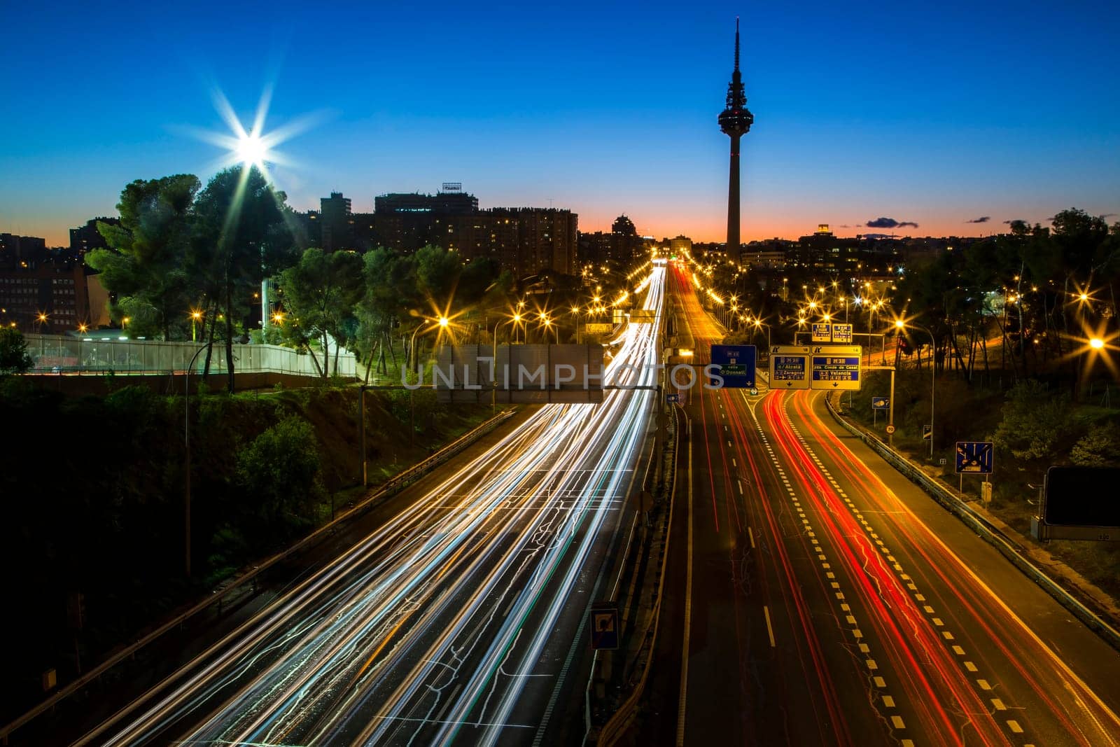 Sunset view of a Madrid skyline with the Torrespaña communications tower in the background and lines of traffic lights.