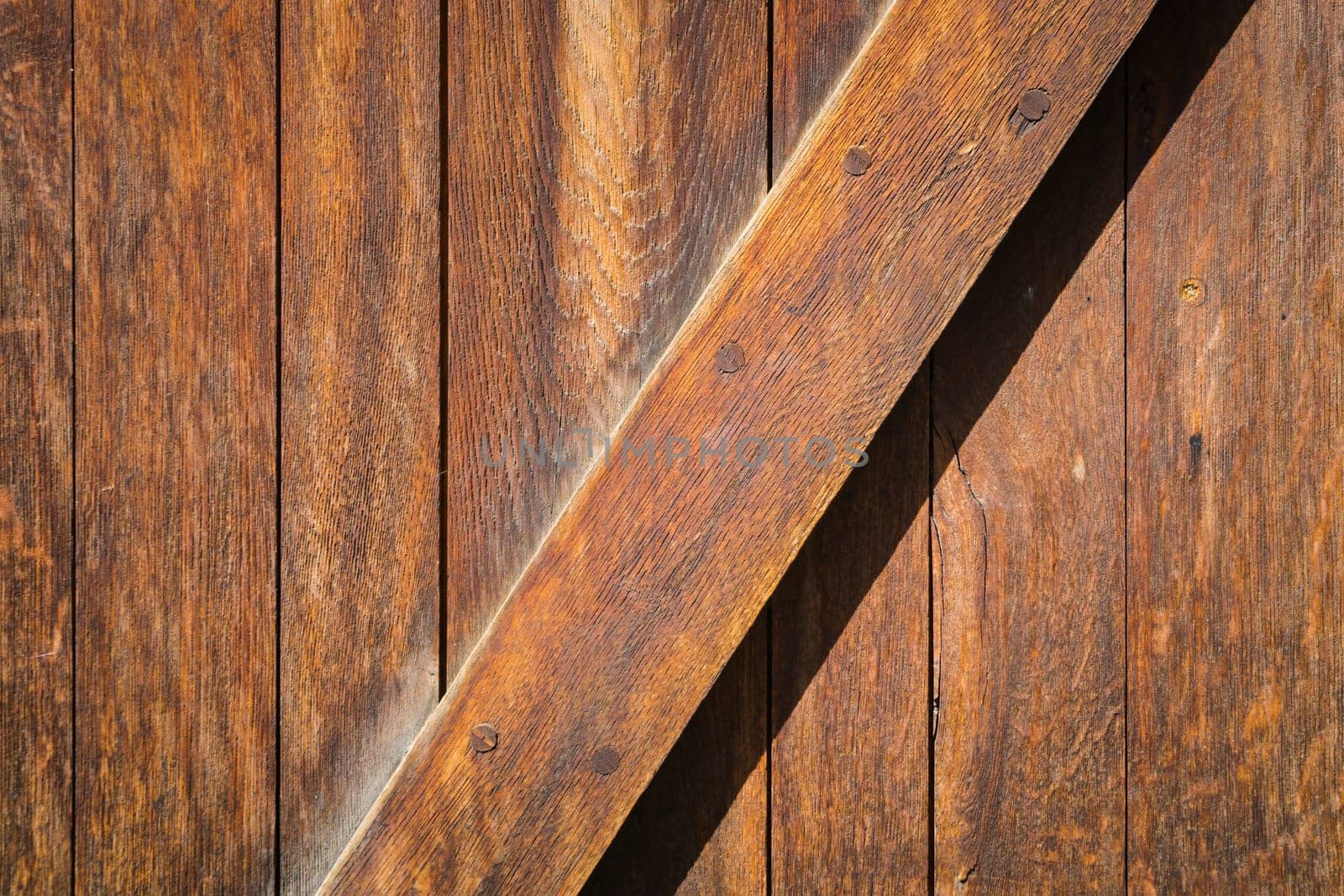 Detail of old unpainted wooden door with vertical slats and one diagonal slat in brown tones.