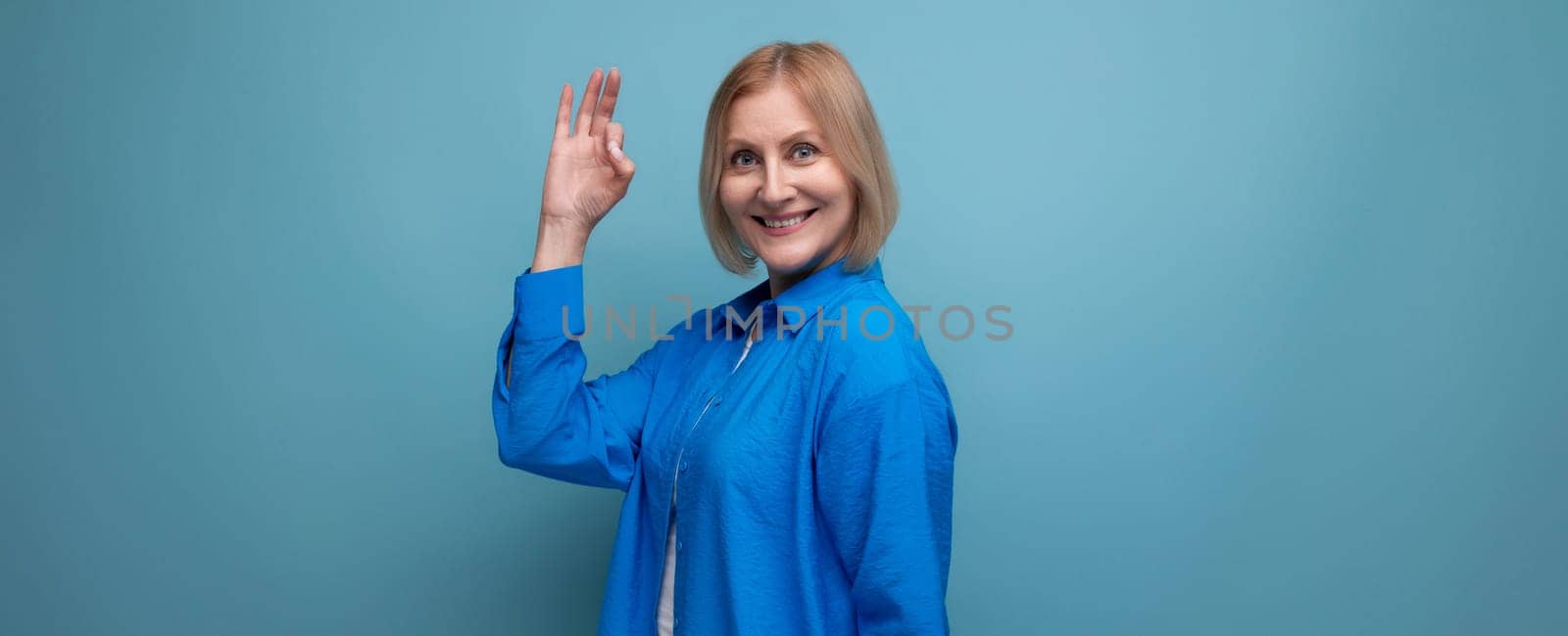 close-up of a mature woman in a blue shirt with an idea on a blue background with copy space by TRMK