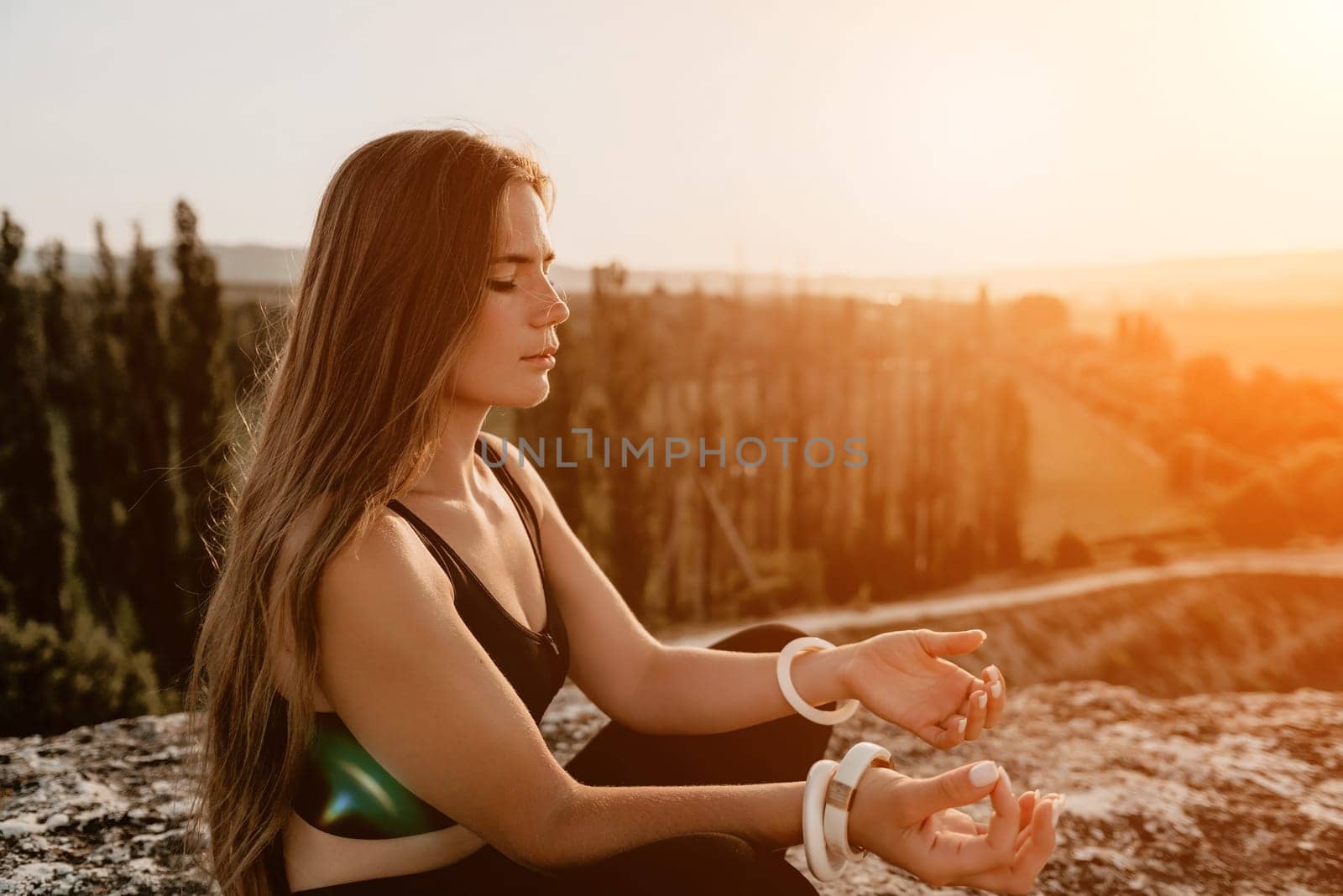 Fitness woman. Happy middle-aged fitness woman doing stretching and pilates on a rock near forest at sunset. Female fitness yoga routine. Healthy lifestyle with focus on well-being and relaxation. by panophotograph