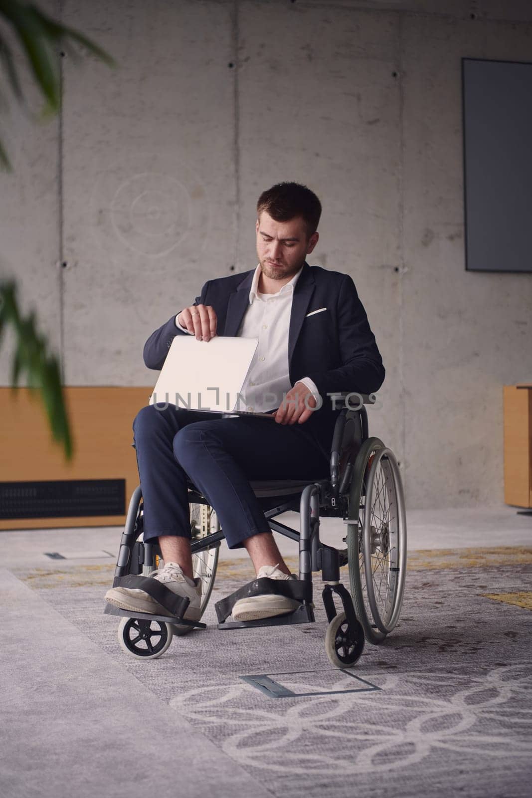 A businessman with disability in a wheelchair using laptop in a modern office . High quality photo