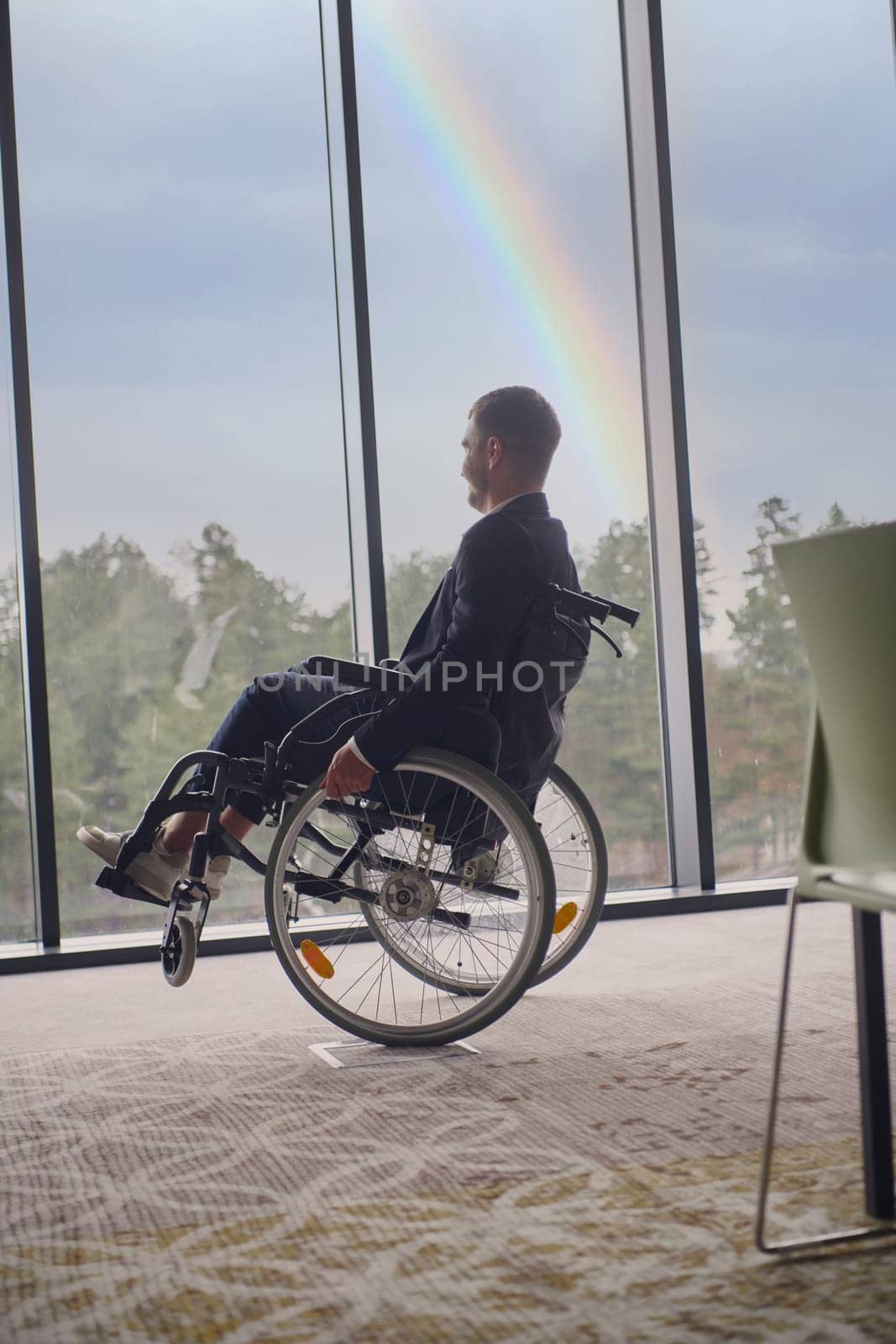 Successful businessman with a disability enjoys a fun-filled moment in his wheelchair, surrounded by the modern ambiance of an inclusive office, while the vibrant rainbow in the background symbolizes diversity and empowerment by dotshock