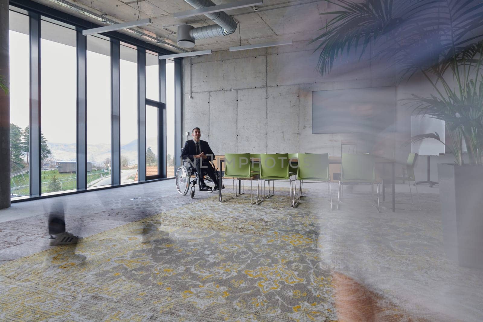 A businessman in a wheelchair sits at a table in a large, modern office, while his colleagues gather around, their steps blurred, symbolizing inclusivity, support, and unity in the face of challenges. by dotshock