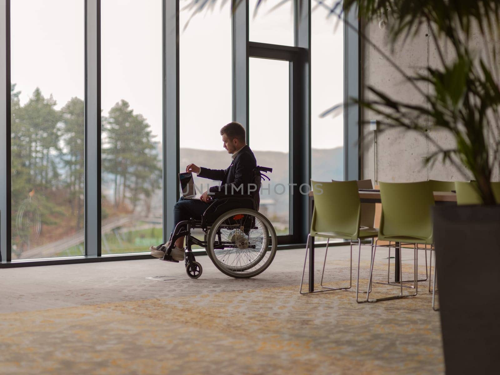 A businessman with disability in a wheelchair using laptop in a modern office . High quality photo