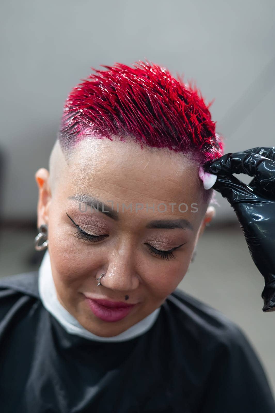 The hairdresser removes excess dye from the skin of a female with a cotton pad.Asian woman with a short haircut in a hairdressing salon