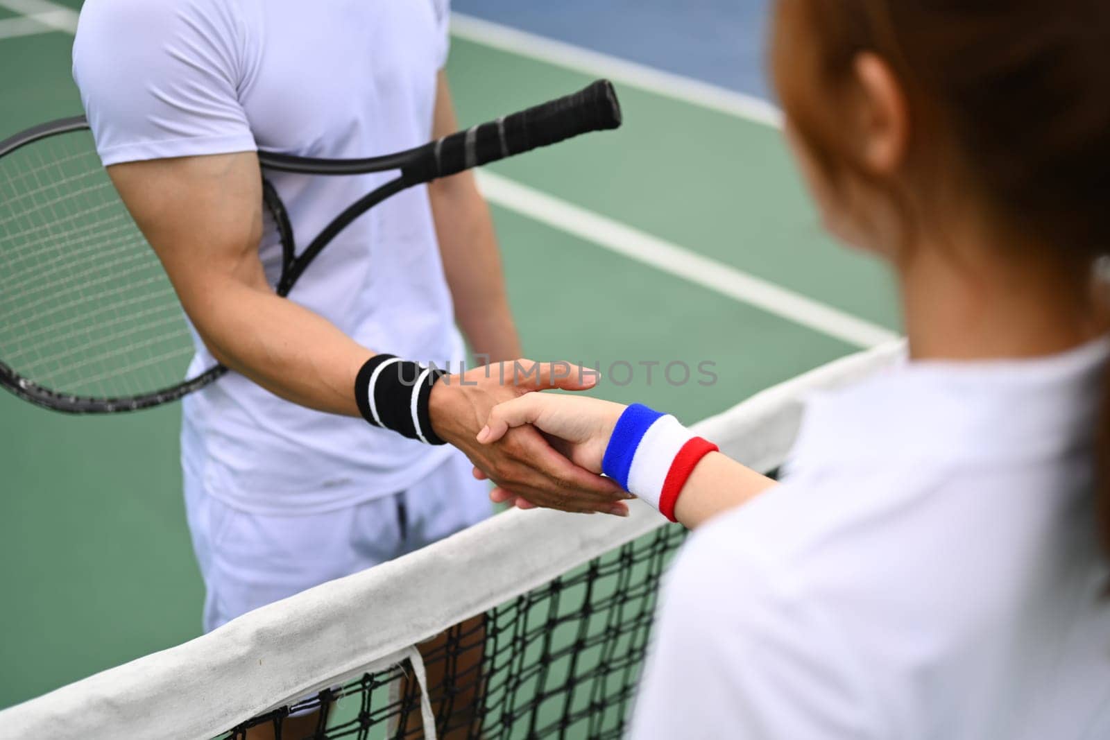 Cropped shot of male and female tennis players shaking hands across net during match at court.