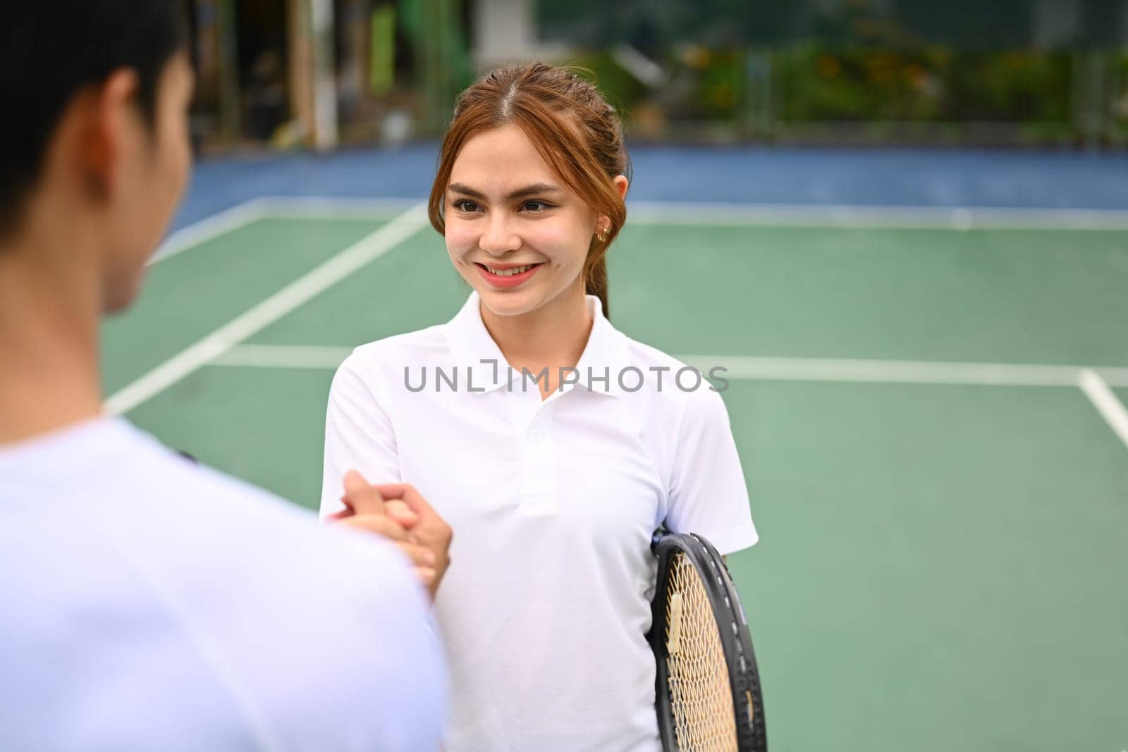 Attractive female tennis players shaking hands with competitor after a competitive match at outdoor court by prathanchorruangsak