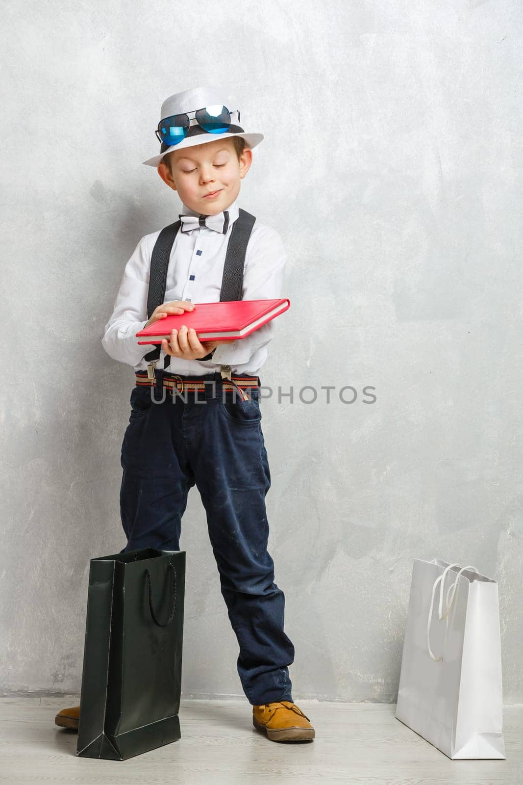 little schoolboy with a book on gray color background.