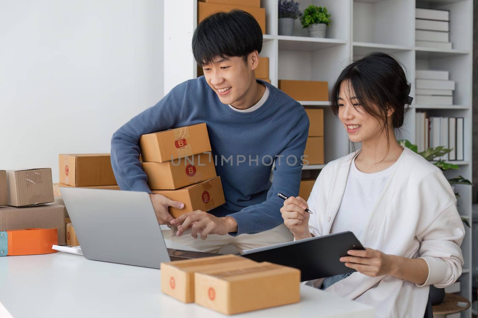 Happy couple people packing parcel boxes, couple lover checking order online on laptop at home by nateemee