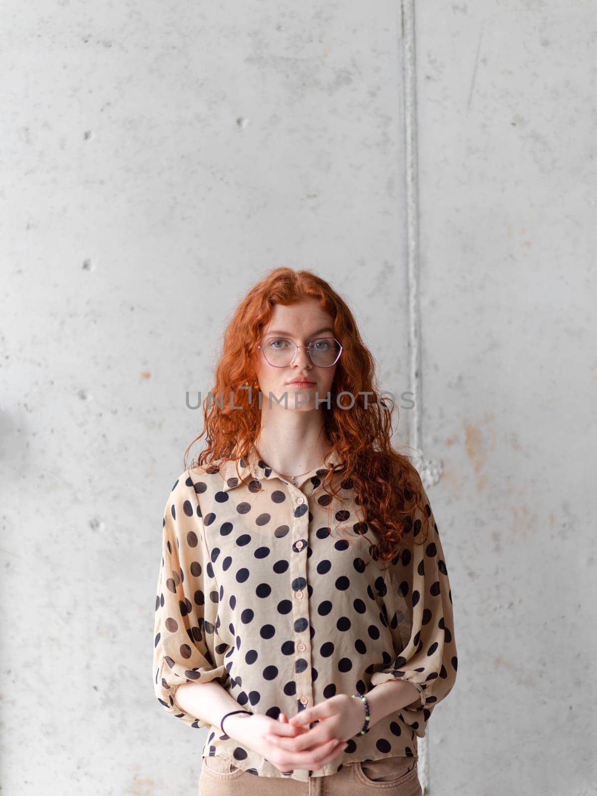 A young entrepreneur with captivating orange hair is striking a confident pose in front of a stylish gray wall