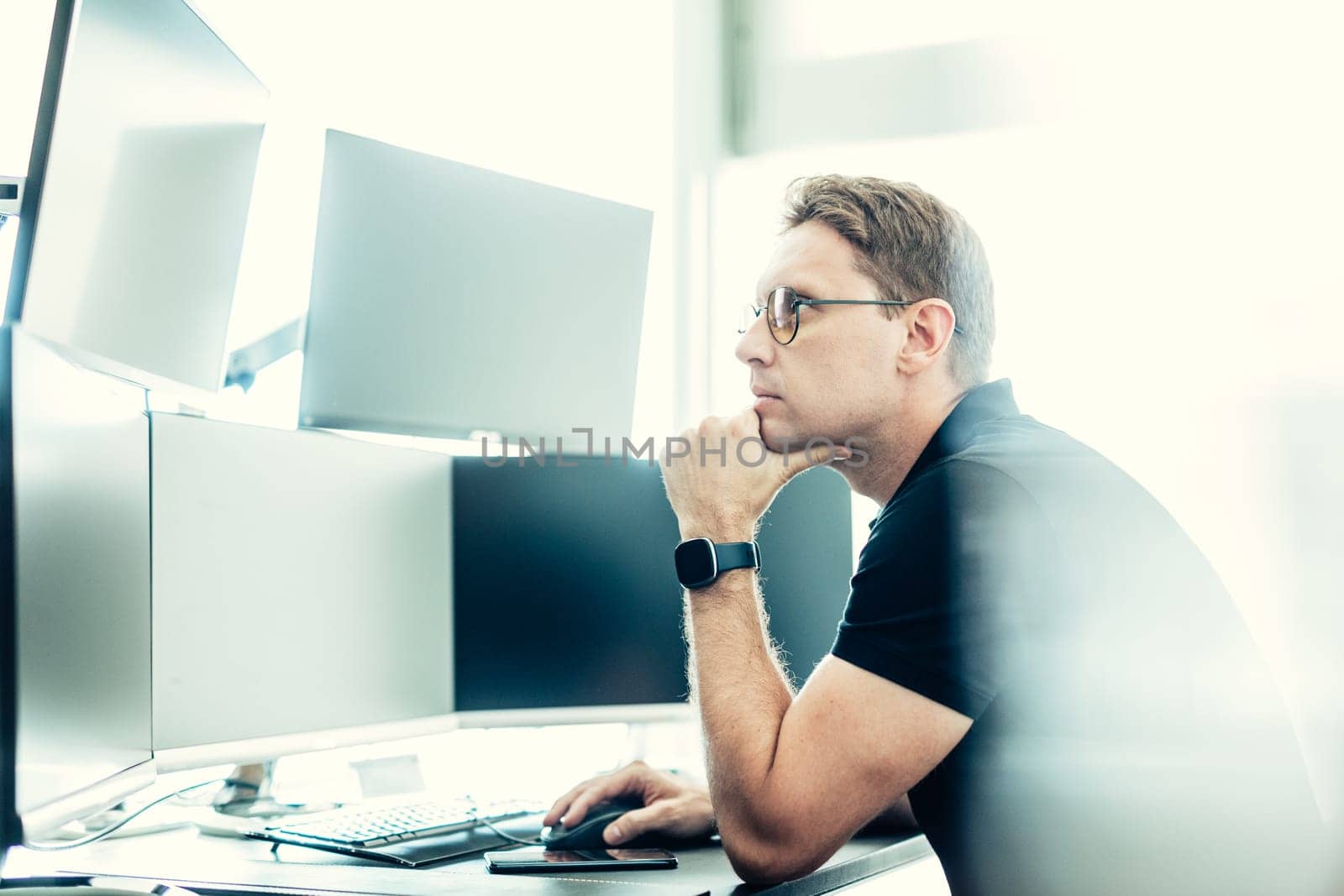 Male stock broker trading online watching charts and data analyses on multiple computer screens.