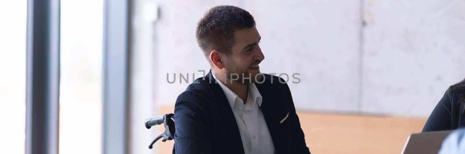 Wide crop photo of wheelchair bound businessman confidently leads a business meeting in a large, modern office, exemplifying inclusive leadership, effective communication, and the power of diversity in driving success and achieving impactful results. by dotshock