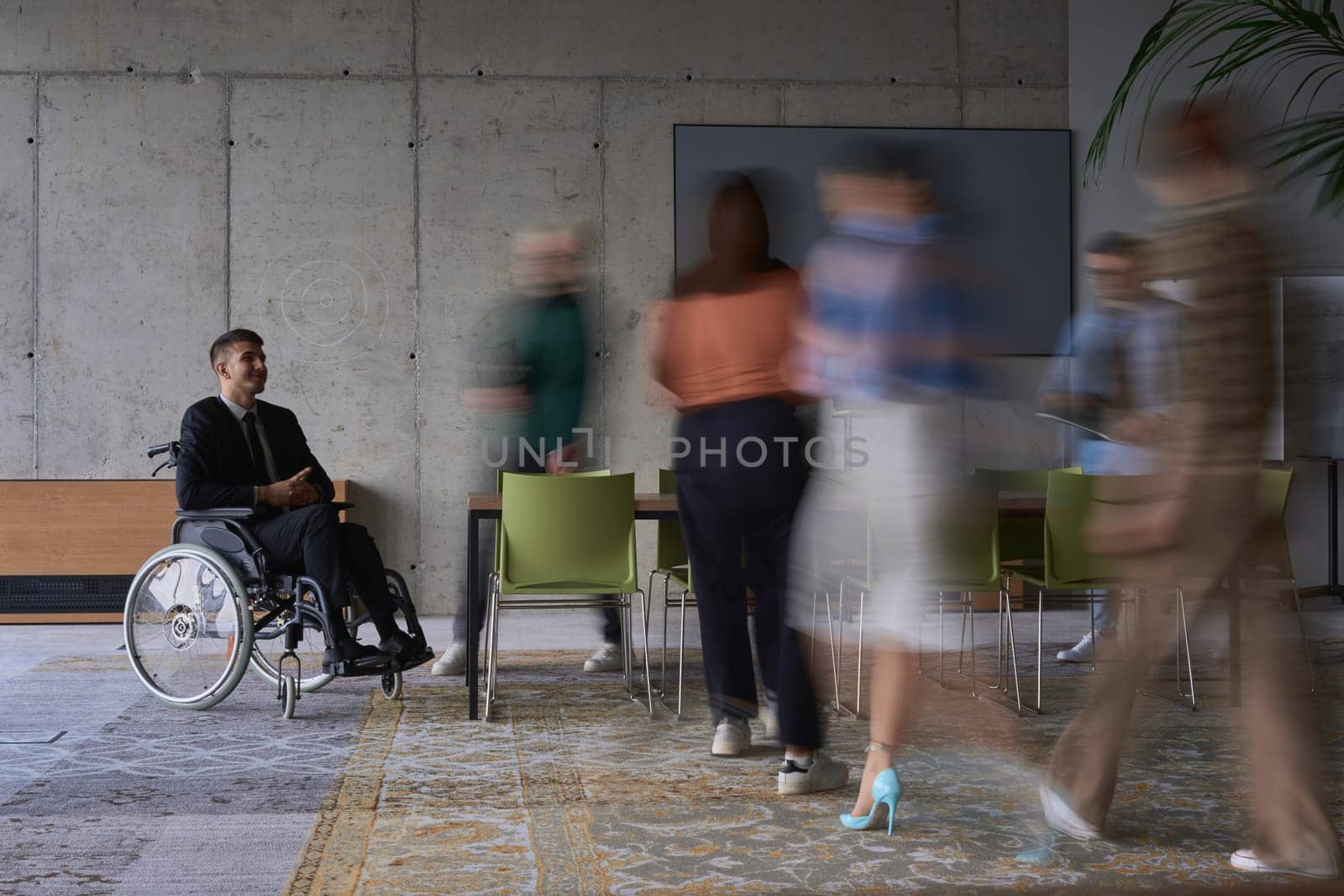 A businessman in a wheelchair in a modern office, surrounded by his colleagues who are portrayed with blurred movements, symbolizing their support and solidarity as they navigate the workspace together