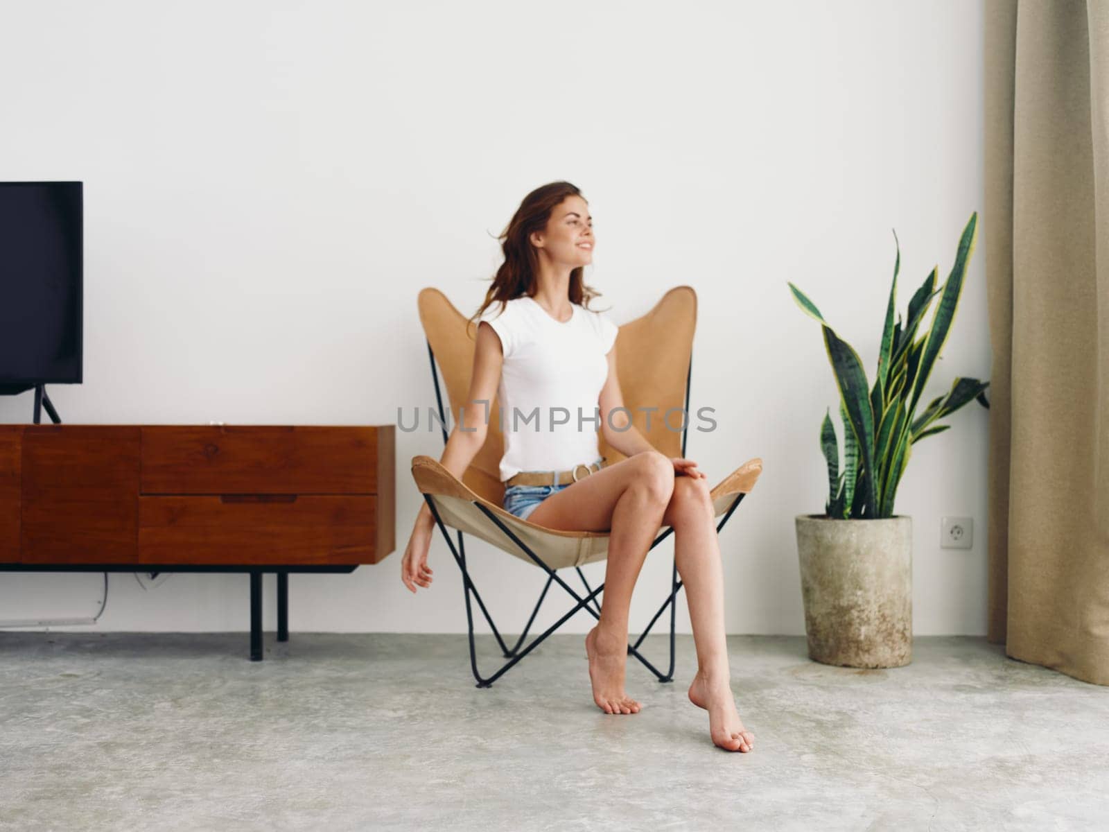 Woman sitting in leather armchair smile with teeth Lifestyle, relaxing at home stylish modern interior with white walls, copy space. by SHOTPRIME