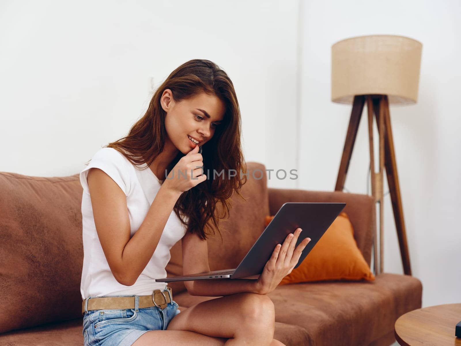 Woman freelancer sitting on the couch with a laptop beautiful smile , modern stylish interior Scandinavian lifestyle, copy space. High quality photo