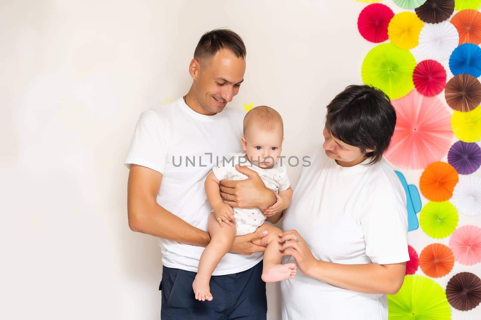 Smiling young mother and father standing at home cradling the cute baby girl in their arms by Andelov13