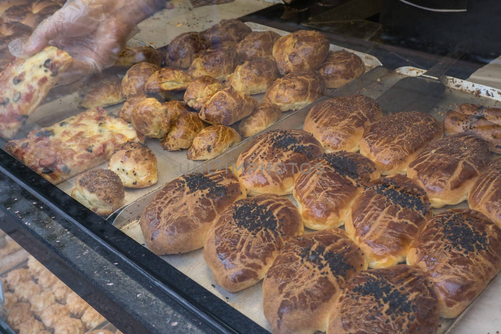 Sweet fresh pastries on the bakery counter are sold and assembled by the baker behind the window pane. European artisan bread shop, retail showcase. by Ekaterina34