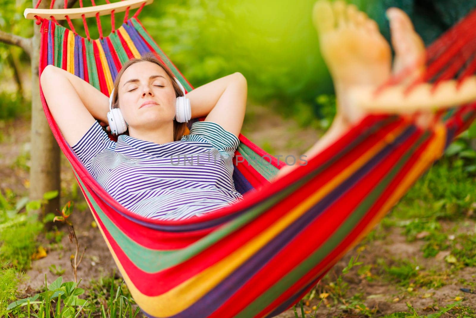 Young woman in headphones listening to music while resting in hammock outdoors by andreyz