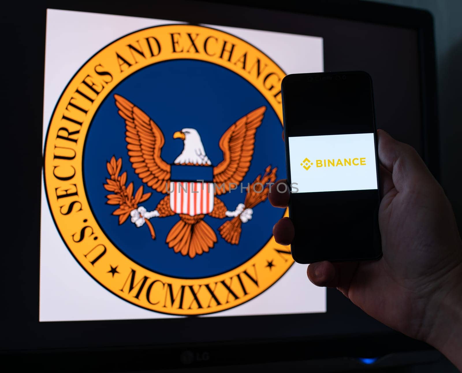 Kyiv, Ukraine - 06 June 2023: Man holds a smartphone with crypto exchange Binance on screen against the background of monitor with the SEC logo. S.E.C. sued on Binance through money laundering in BNB