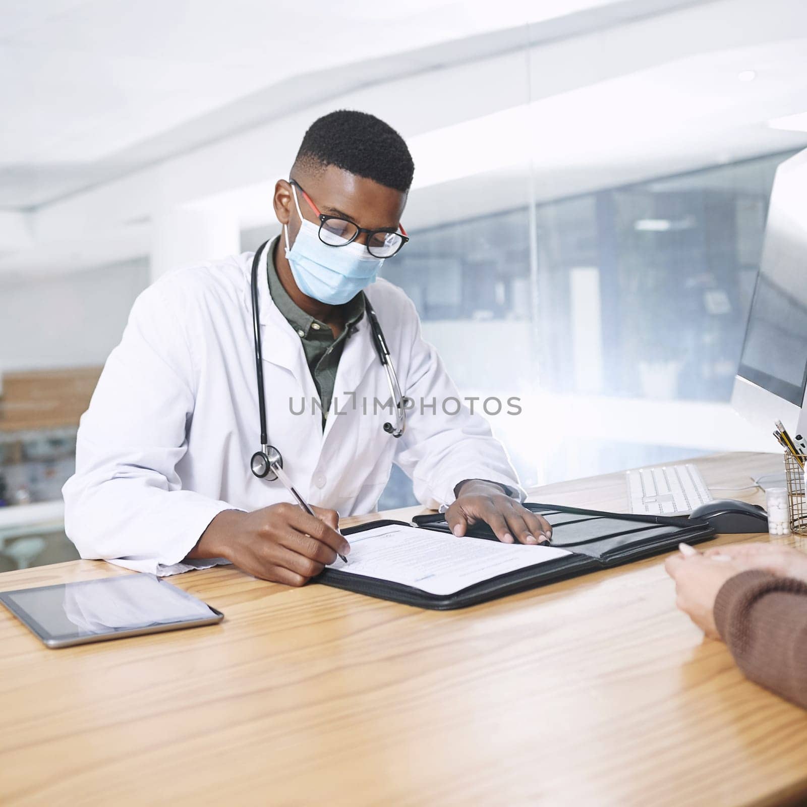 I want to do a few more blood tests. a young doctor sitting with his patient and wearing a mask while writing a prescription during a consultation. by YuriArcurs