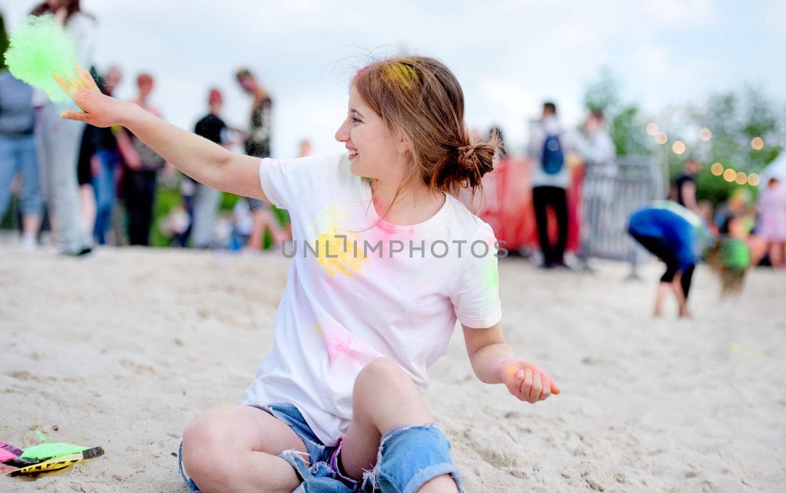 Pretty girl in indian traditional Holi festival sitting at beach sand with colorful powder and having fun. Female teenager enjoying positive holiday