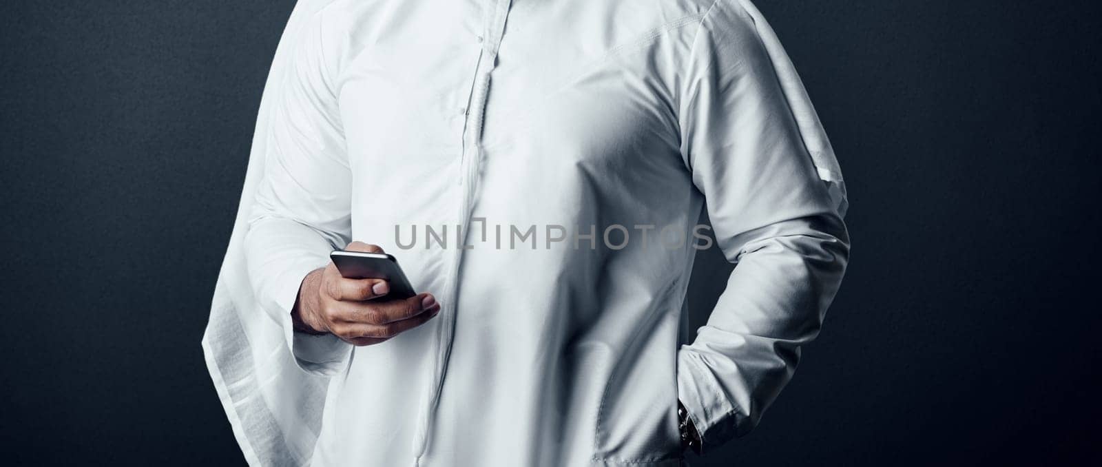 Accessing information for his work anywhere. Studio shot of an unrecognizable man dressed in Islamic traditional clothing posing against a dark background. by YuriArcurs