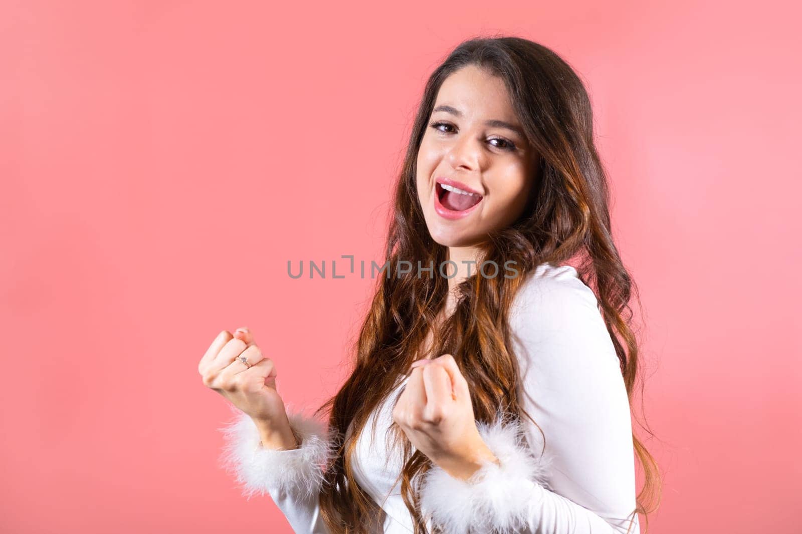 Young woman showing funny dance moves enjoys party. Brown-haired lady smiles happily with life at pink wall studio
