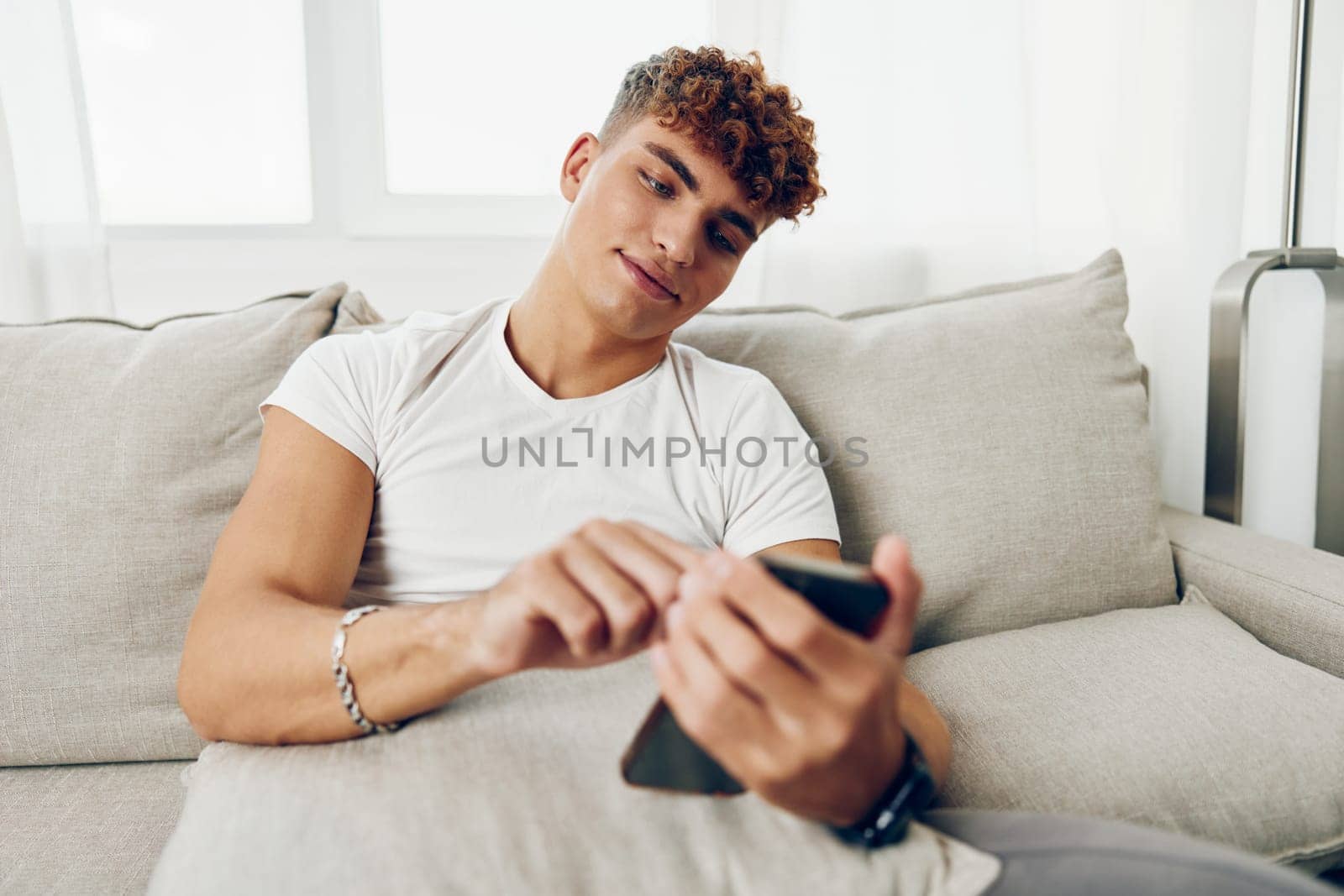man interior text message curly smart laptop sofa mobile sitting cell internet mockup lifestyle phone young male adult freelancer using