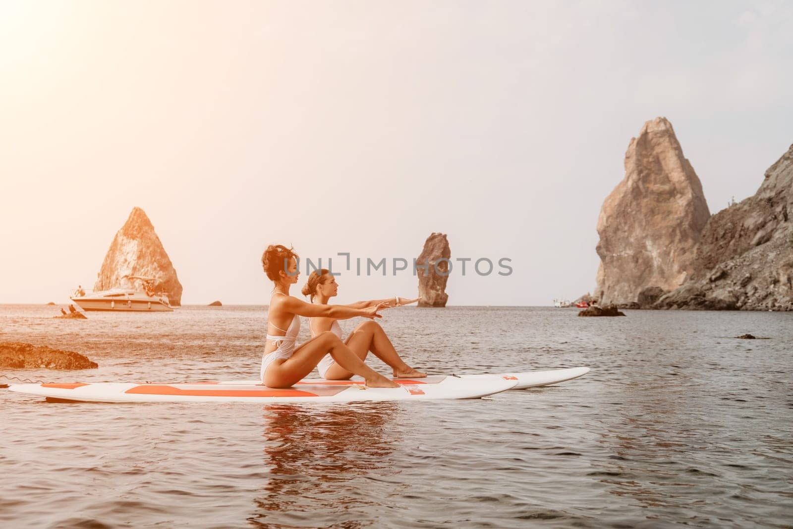 Woman sup yoga. Middle age sporty woman practising yoga pilates on paddle sup surfboard. Female stretching doing workout on sea water. Modern individual hipster outdoor summer sport activity