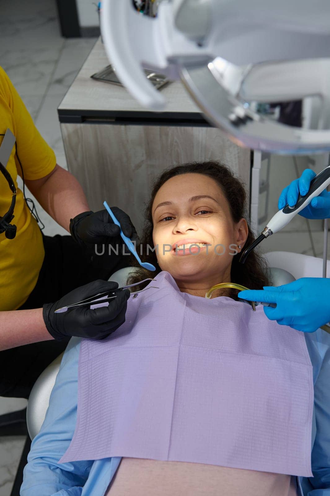 Beautiful pregnant woman in dental chair getting oral cavity examination and treatment in dentistry clinic. Professional dentist and assistant holding instruments near a female patient face. Top view