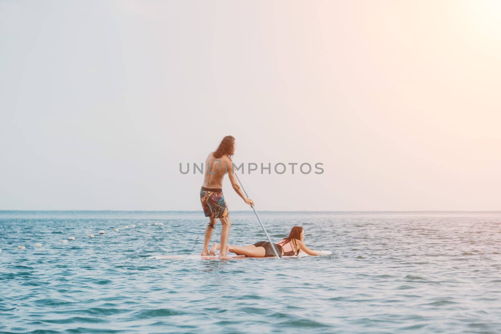 Silhouette of woman standing, surfing on SUP board, confident paddling through water surface. Idyllic sunset or sunrise. Sports active lifestyle at sea or river.