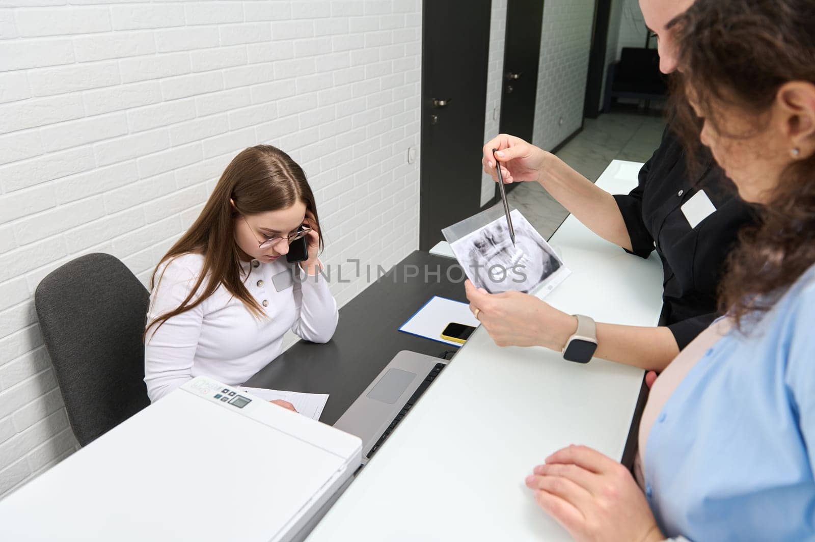 Female patient stands near a dentist holds teeth X-ray image, explains treatment that needs to perform in dental clinic by artgf