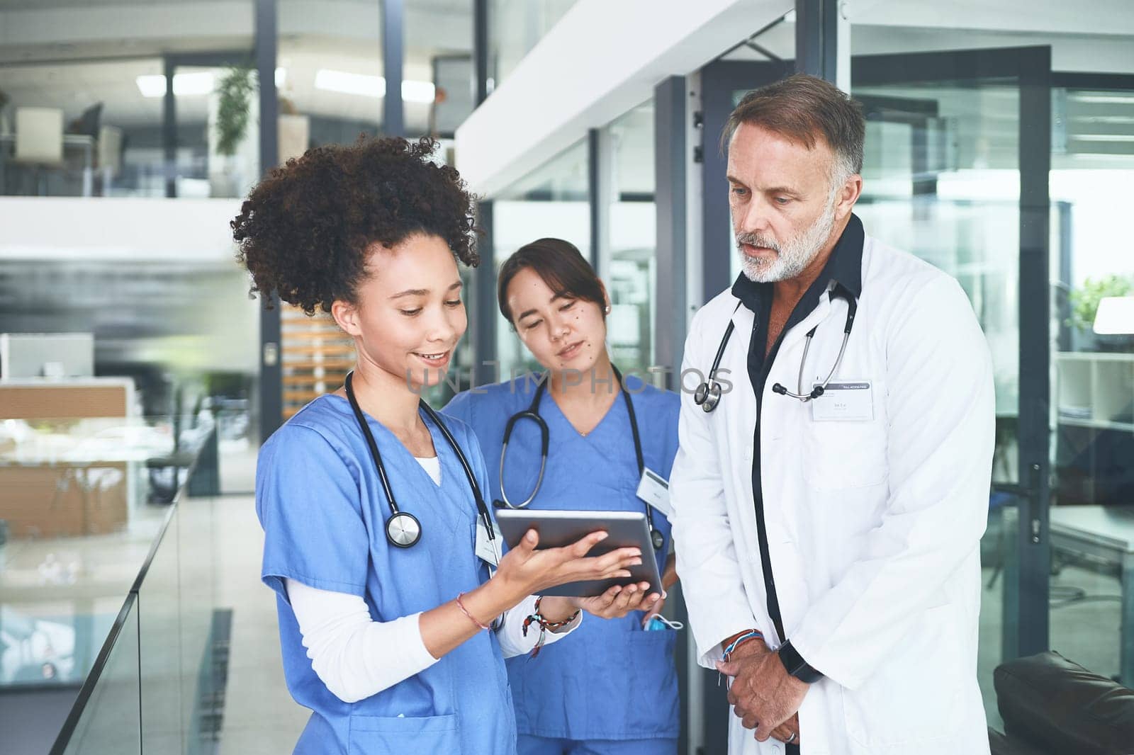 Communication breeds results. a handsome mature doctor standing with his nurses and using a digital tablet during a discussion. by YuriArcurs