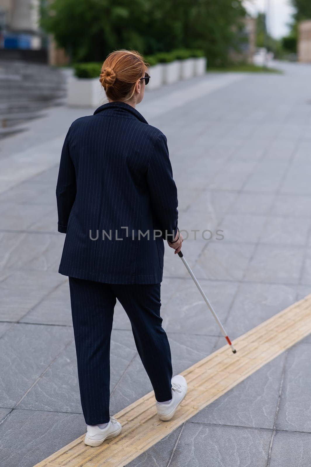 Blind businesswoman walking along tactile tiles with a cane. by mrwed54