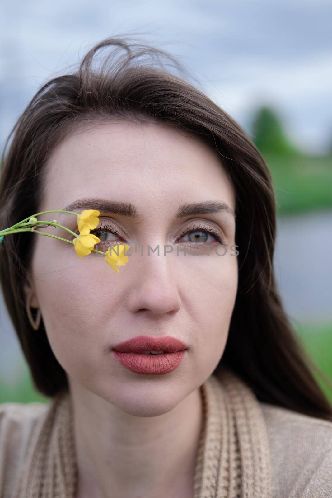 portrait of beautiful brunette woman with yellow small wildflower. skin care, nature.