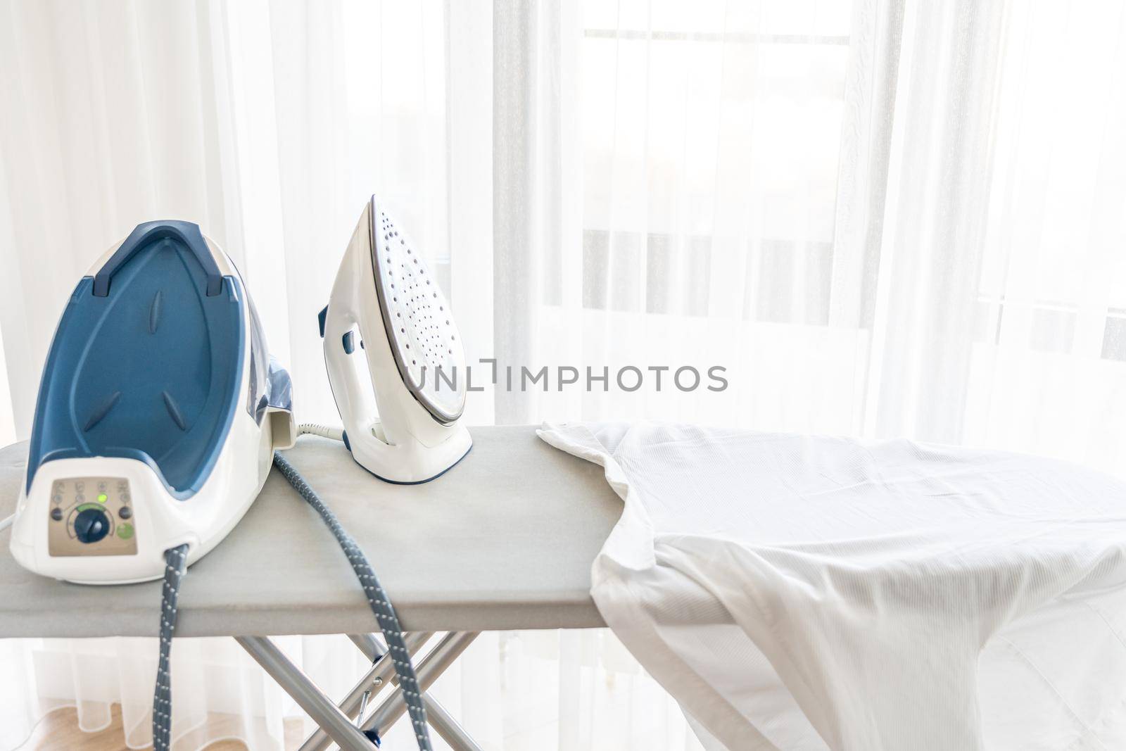 Steam generator iron standing on ironing board near panoramic window
