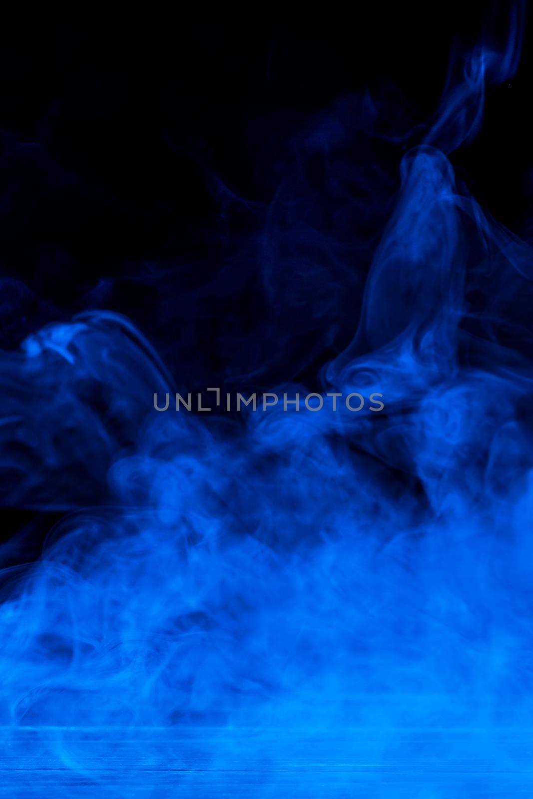 Conceptual image of blue smoke isolated on dark black background and wooden table.