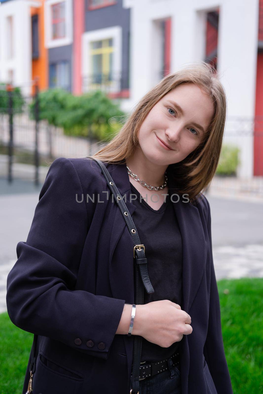 portrait of confident attractive brunette woman in black on background of colorful bright buildings. business woman. feminine. millennial people.