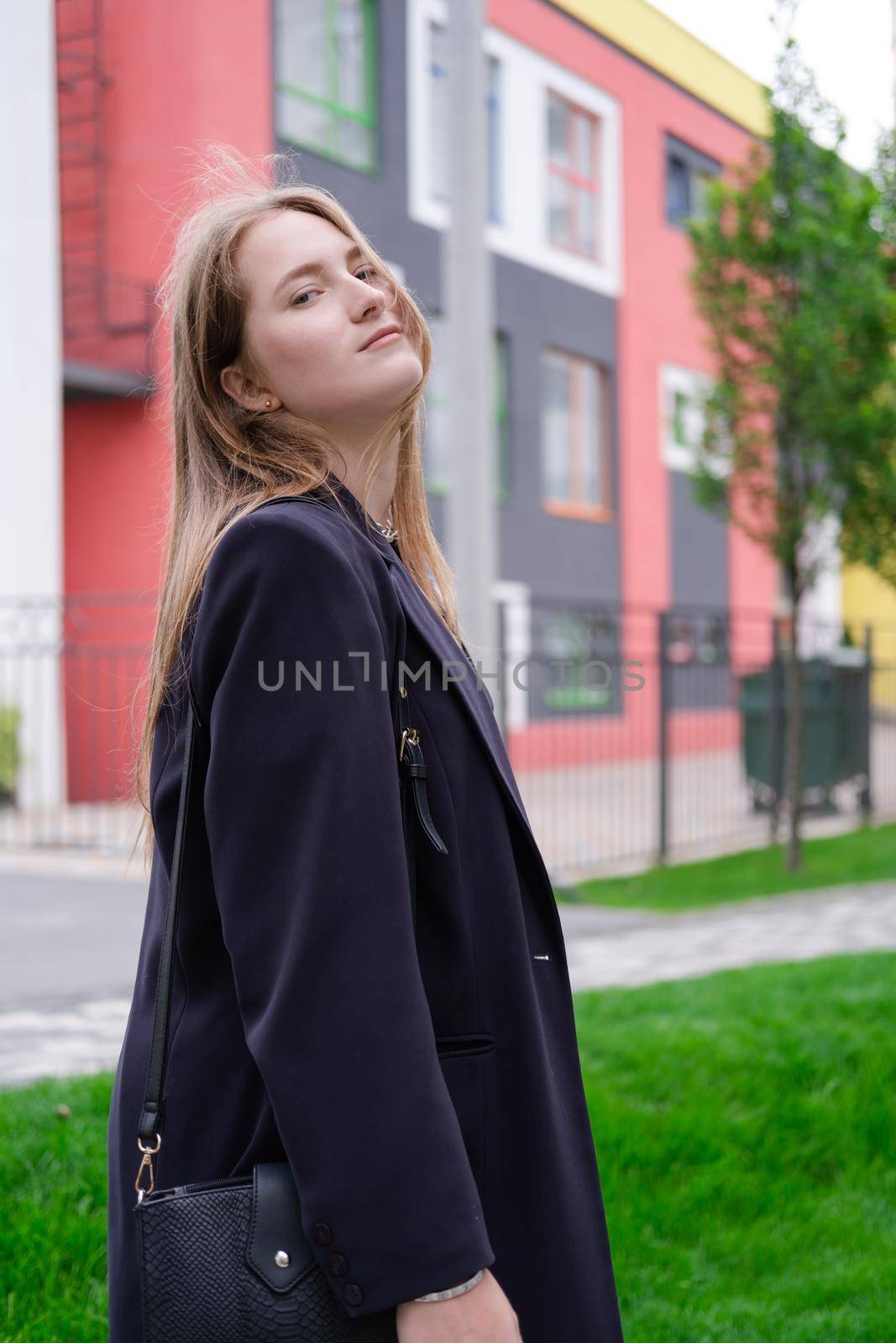 portrait of confident attractive brunette woman in black on background of colorful bright buildings. business woman. feminine. millennial people.