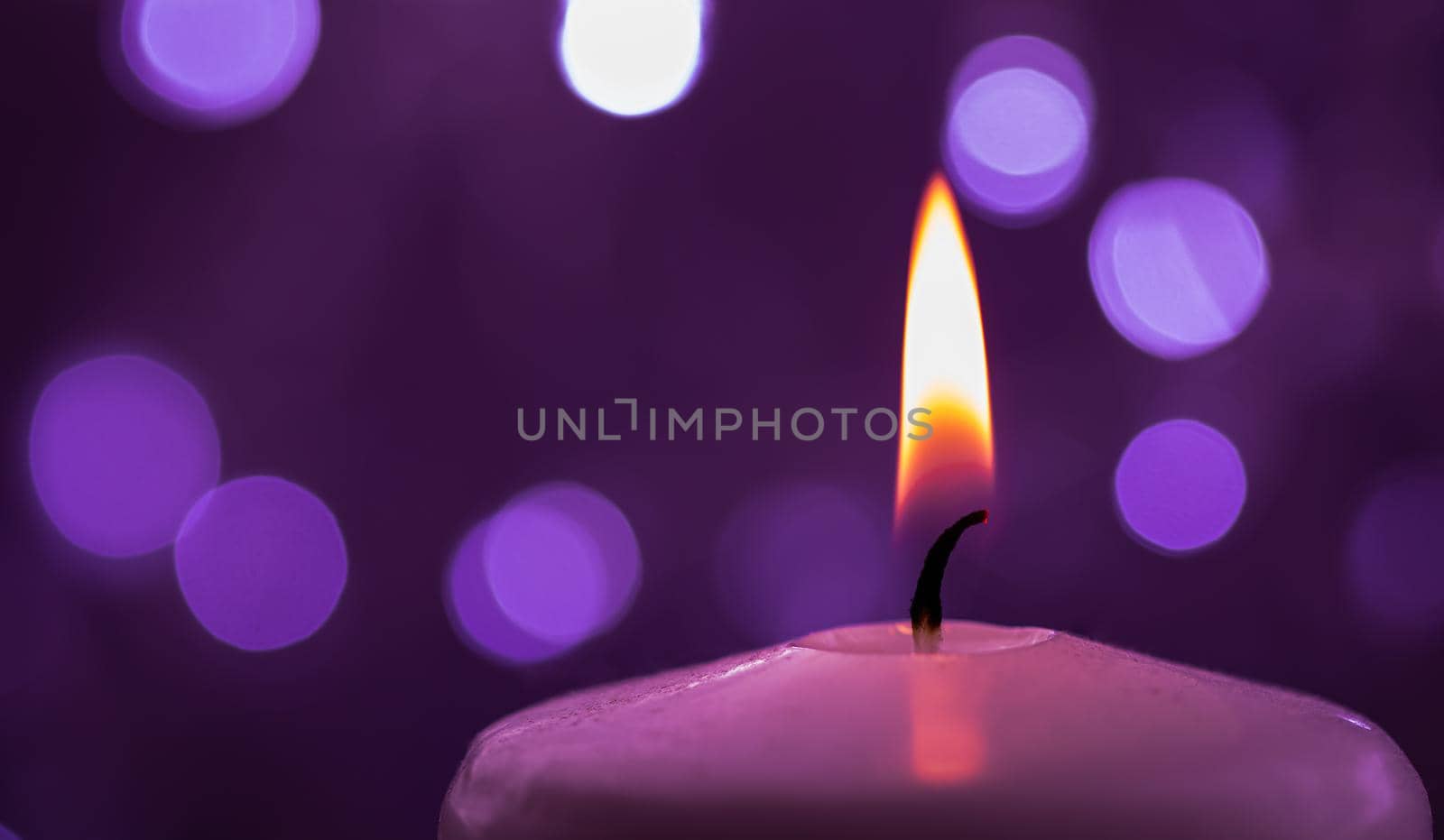 Close up of one burning candle with blurred Christmas light background.