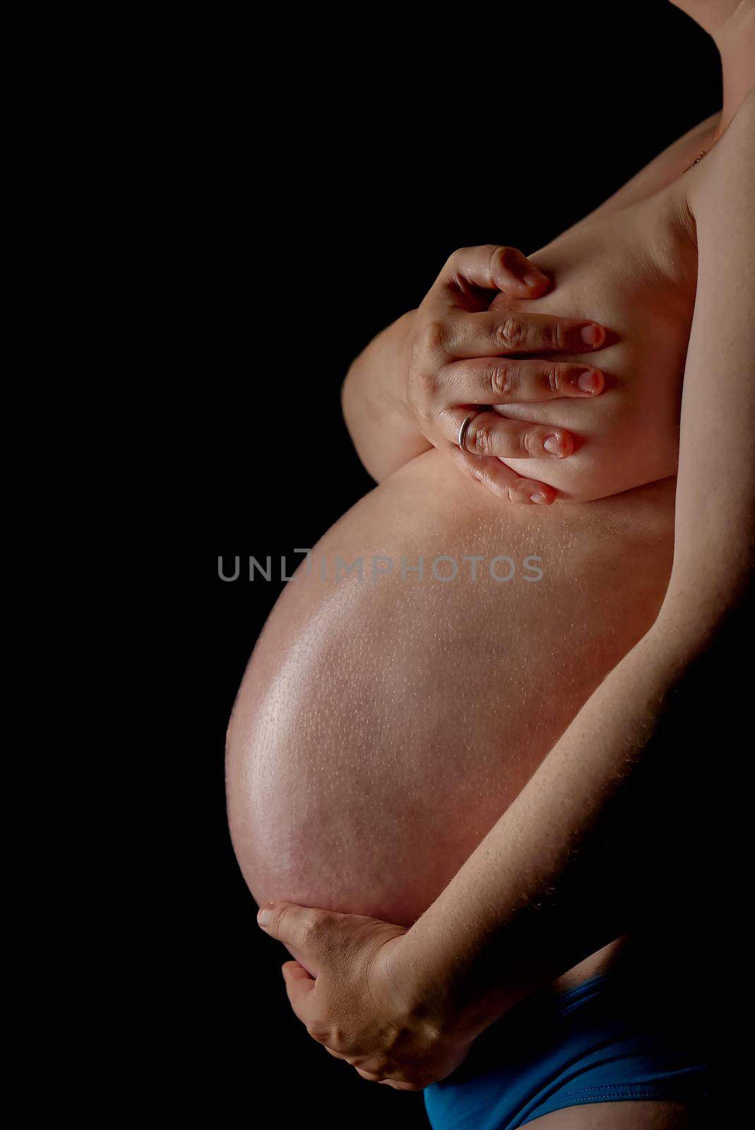 Belly of a pregnant woman on the black background. Belly of a pregnant woman in low key. Body of a 9-month pregnant woman. 40 weeks pregnant women infront of black backdrop