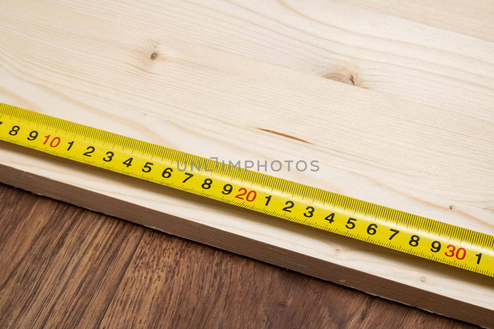 Measuring a wooden board with an yellow tape measure close up