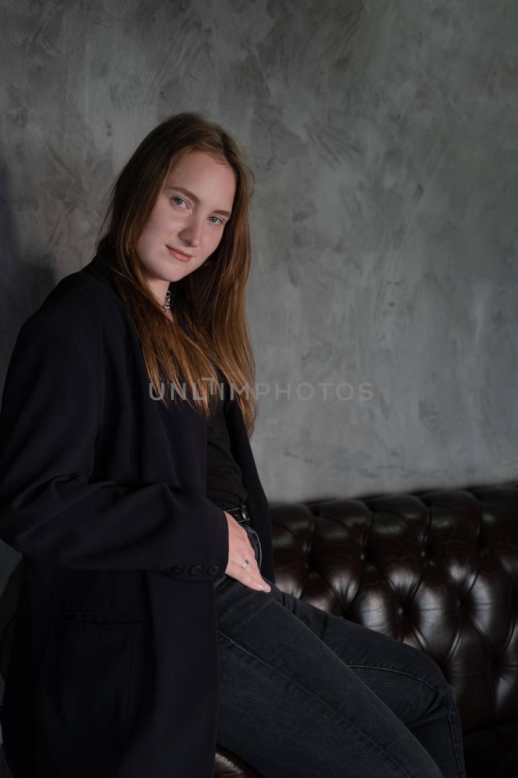 portrait of beautiful confident brunette woman in black in grey dark room. business woman. feminine. millennial people. stylish fashion clothes.