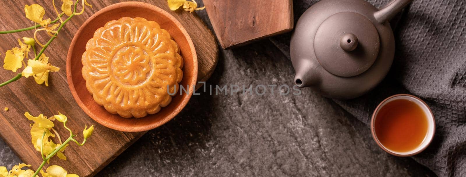 Mid-Autumn Festival traditional food concept - Beautiful Moon cake on black slate table with tea, pastry mold, flower, top view, flat lay, copy space